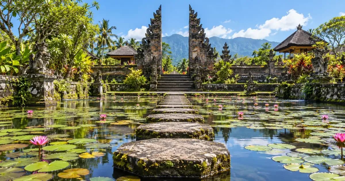 Wide view of an entrance path of stepping stones across a shallow lily pond in Bali, weathered volcanic stone and moss in the foreground, in bright midday light.